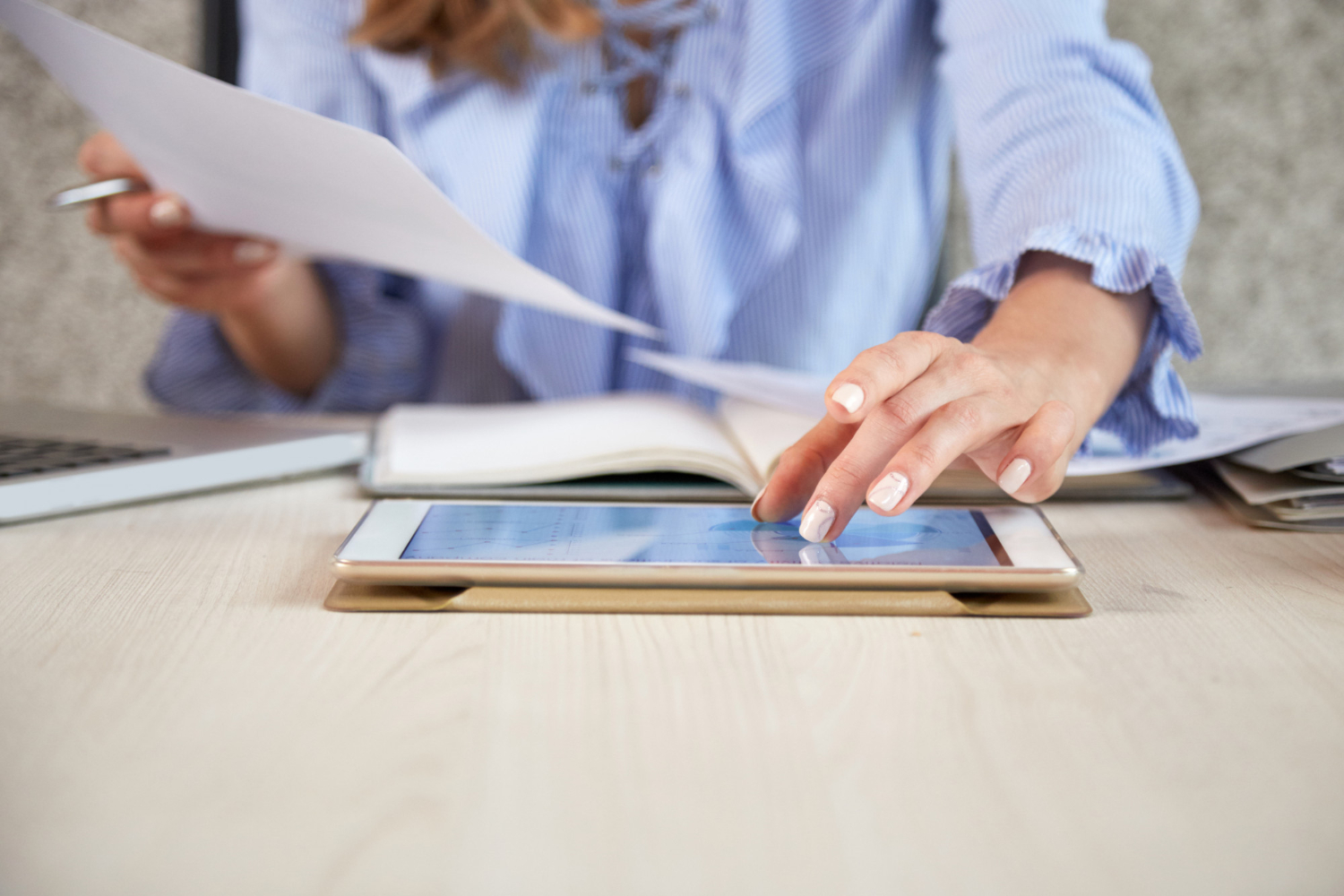 donna in ufficio con fogli in mano digita su un tablet