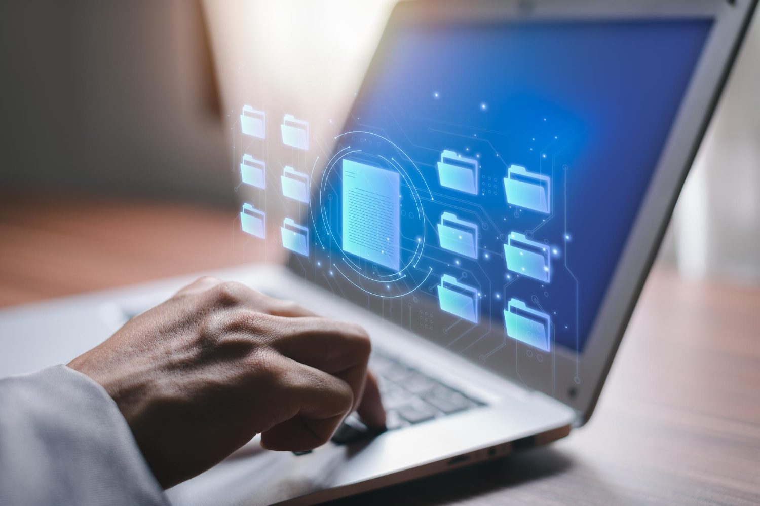 Mani maschili che digitano sulla tastiera di un laptop dal cui schermo vengono fuori delle icone di cartelle
